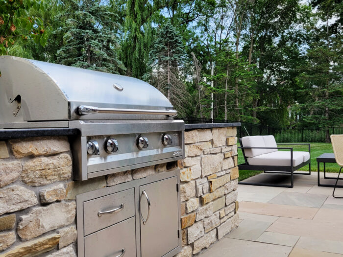 back yard grill with natural stone island and matching stone paver patio