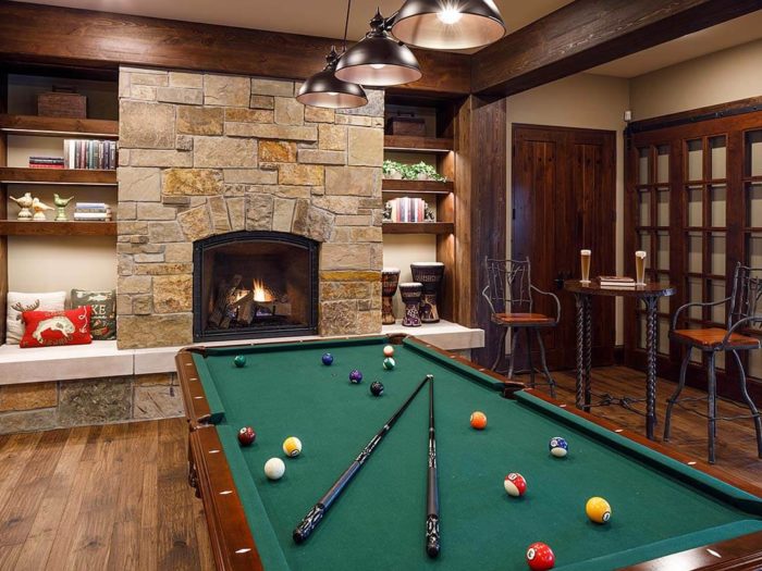 Rec room with pool table and adjacent fireplace featuring natural stone with shades of tan, brown, and gold.