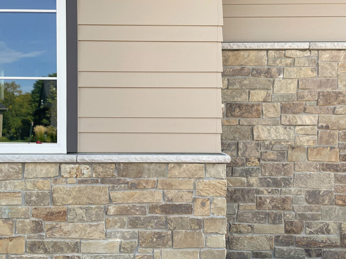 photo of a tan home with a brown and tan natural stone veneer wainscot