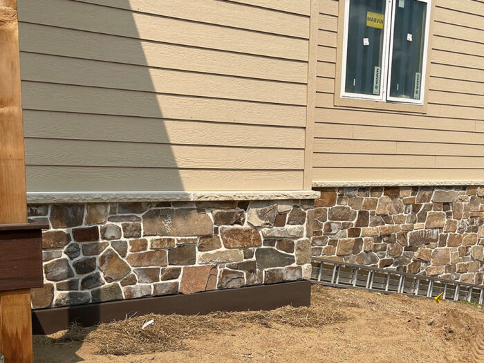elk mountain natural stone veneer wainscot installed on a home below tan-colored siding.