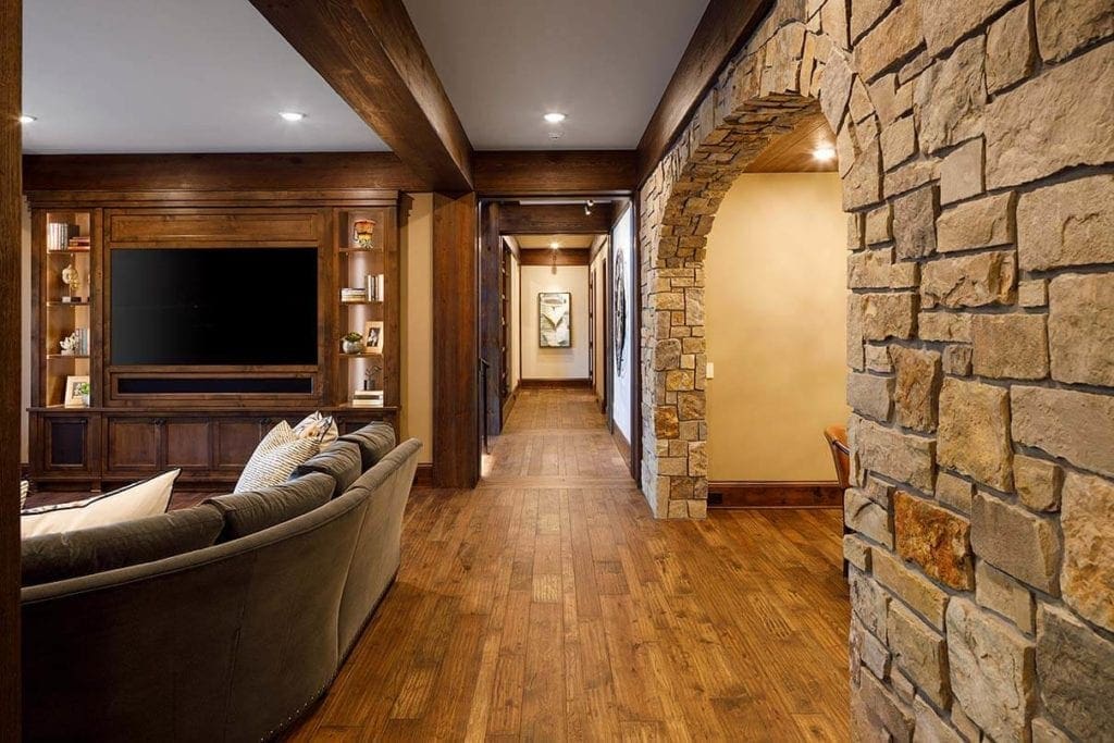 View down hallway with wood floors, a tan-colored natural stone archway on the right, and TV viewing area on the left.