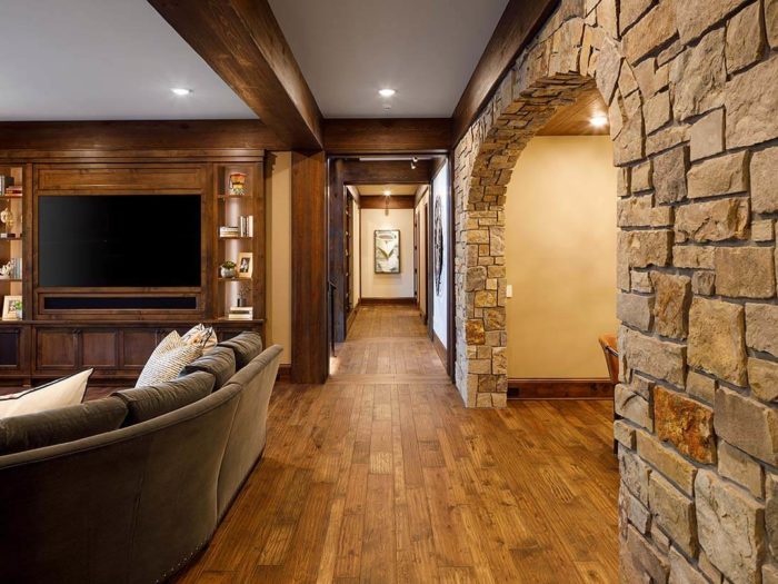 View down hallway with wood floors, a tan-colored natural stone archway on the right, and TV viewing area on the left.